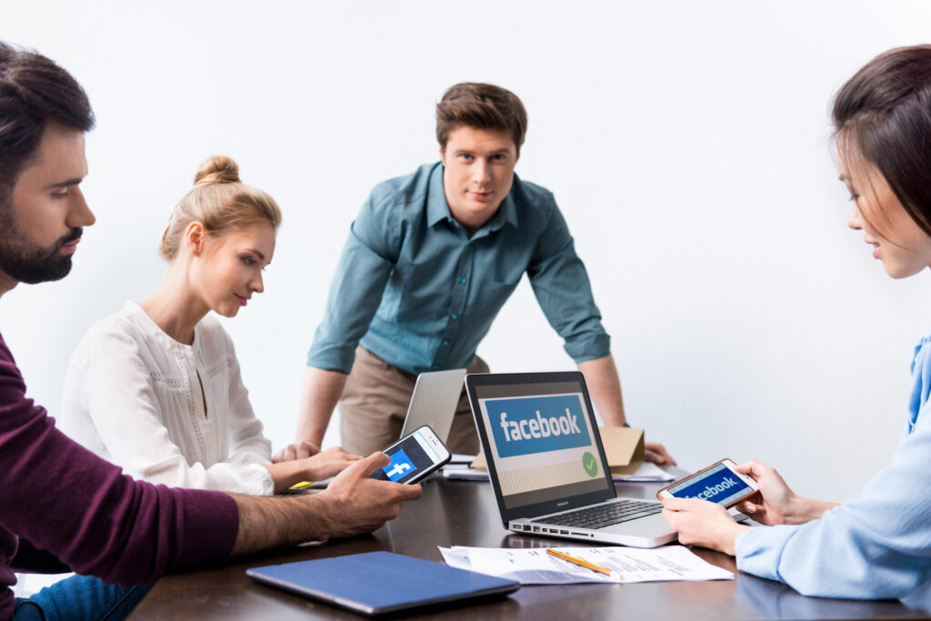 Young businesspeople using digital devices with facebook logo icons on screens